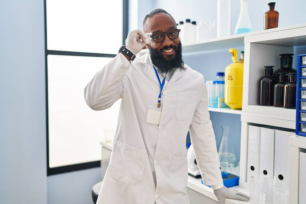 Young african american man wearing scientist uniform standing at laboratory - 写真・画像