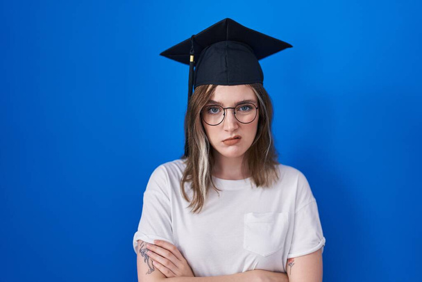 Blonde caucasian woman wearing graduation cap skeptic and nervous, disapproving expression on face with crossed arms. negative person.  - 写真・画像