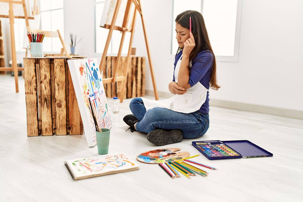 Молодая латиноамериканка с сомнительным выражением лица рисует в художественной студии - Фото, изображение