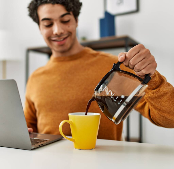 Молодий іспаномовний чоловік використовує ноутбук і п'є каву вдома
. - Фото, зображення