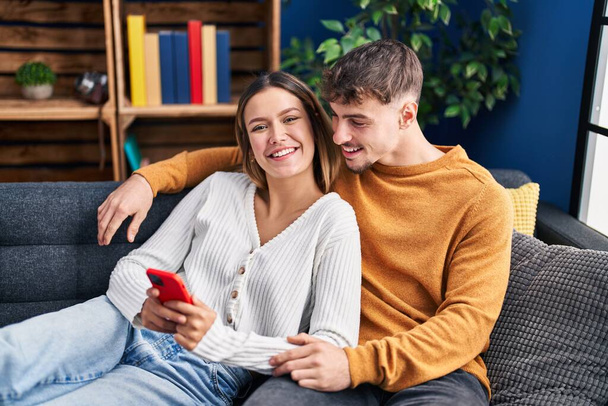 Young man and woman couple using smartphone sitting on sofa at home - Foto, imagen