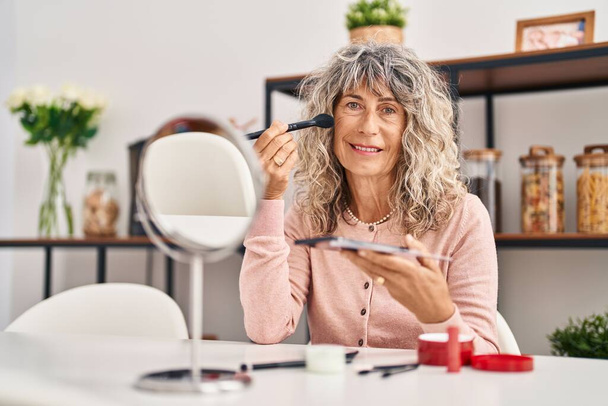 Μέση ηλικία γυναίκα χαμογελώντας αυτοπεποίθηση εφαρμογή μακιγιάζ στο σπίτι - Φωτογραφία, εικόνα