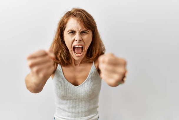 Beautiful caucasian woman standing over isolated background angry and mad raising fists frustrated and furious while shouting with anger. rage and aggressive concept.  - Foto, Imagem
