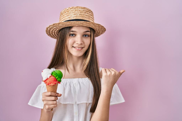 Teenager girl holding ice cream pointing to the back behind with hand and thumbs up, smiling confident  - Foto, Imagen