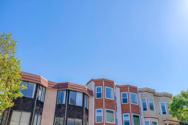 Rowhouses with bay windows against the clear sky in San Francisco, CA. There are two houses from the left with black left and brown center wood sidings beside the beige house on the right. - Foto, Imagem