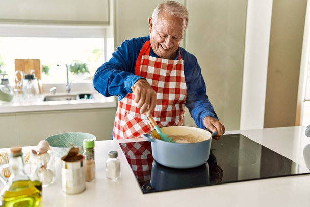 Senior man glimlacht zelfverzekerd koken spaghetti in de keuken - Foto, afbeelding
