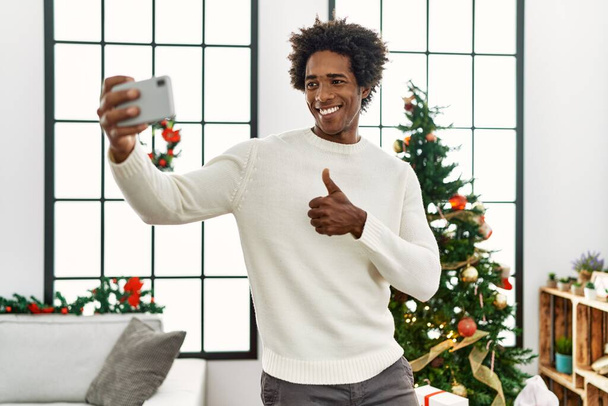 若いですアフリカ系アメリカ人男性作る自撮りによってザスマートフォンスタンドによってクリスマスツリーにホーム. - 写真・画像