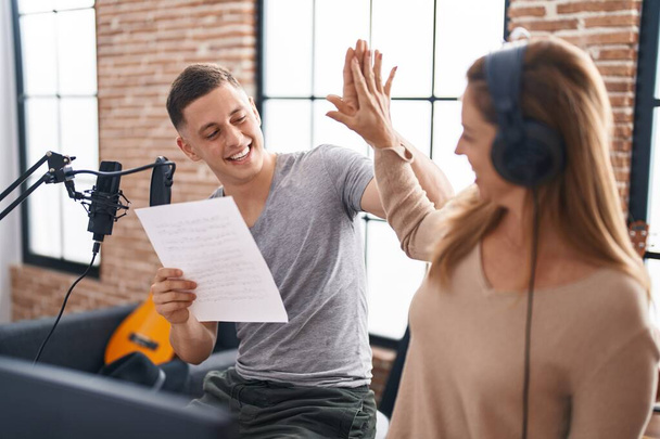 Man and woman musicians singing song high five with hands raised up at music studio - Photo, Image