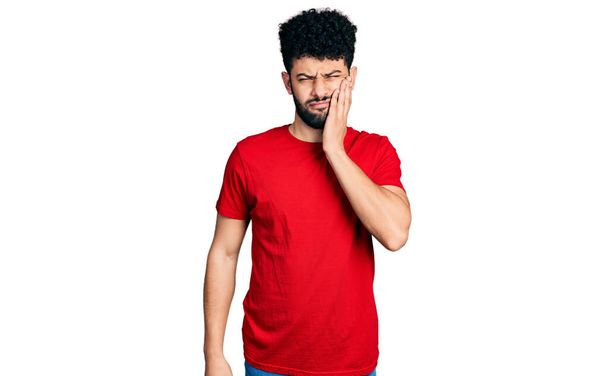 Молодий арабський чоловік з бородою в повсякденній червоній сорочці торкається рота з болючим виразом через зубний біль або стоматологічні захворювання на зубах. стоматолог
  - Фото, зображення