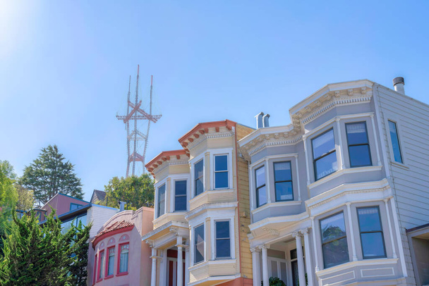 View of rowhouses and Sutro Tower from below at San Francisco, CA. There are two houses on the right with bay windows and decorative porch columns near the house on the left with curved walls. - Zdjęcie, obraz