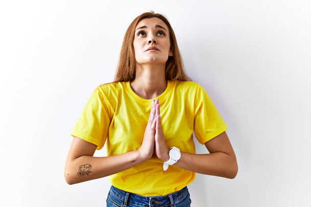 Jonge brunette vrouw staan over geïsoleerde achtergrond bedelen en bidden met de handen samen met hoop uitdrukking op het gezicht zeer emotioneel en bezorgd. bedelen.  - Foto, afbeelding