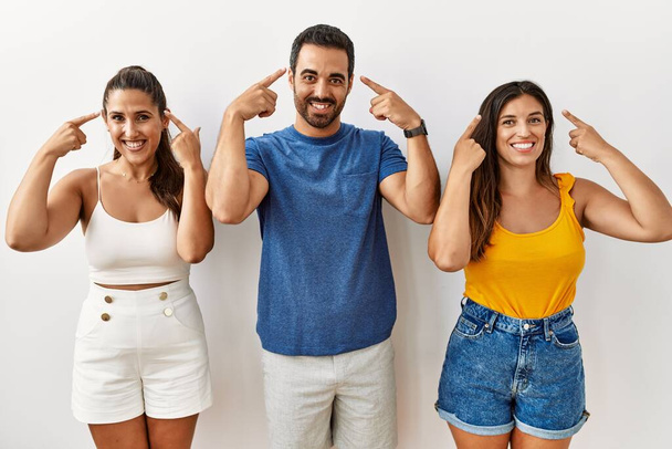 Skupina mladých hispánců, kteří stojí nad izolovaným pozadím a usmívají se ukazujíce na hlavu oběma prsty, skvělý nápad nebo myšlenka, dobrá paměť  - Fotografie, Obrázek