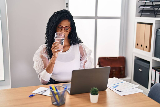 African American επιχειρηματίας γυναίκα χρησιμοποιώντας φορητό υπολογιστή πόσιμο ποτήρι νερό στο γραφείο - Φωτογραφία, εικόνα