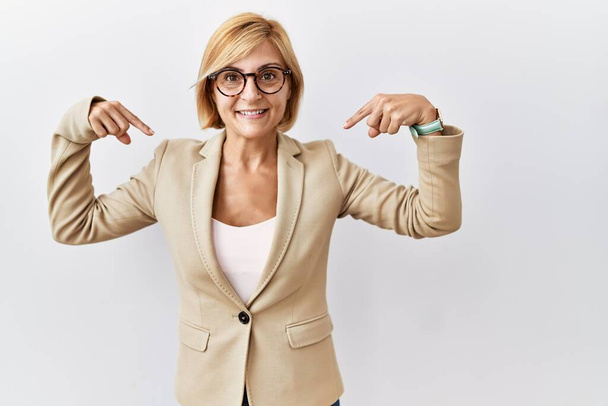 Middle age blonde business woman standing over isolated background looking confident with smile on face, pointing oneself with fingers proud and happy.  - Photo, Image