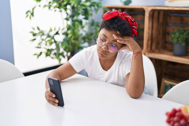 African american woman using smartphone with serious expression at home - Foto, Imagem