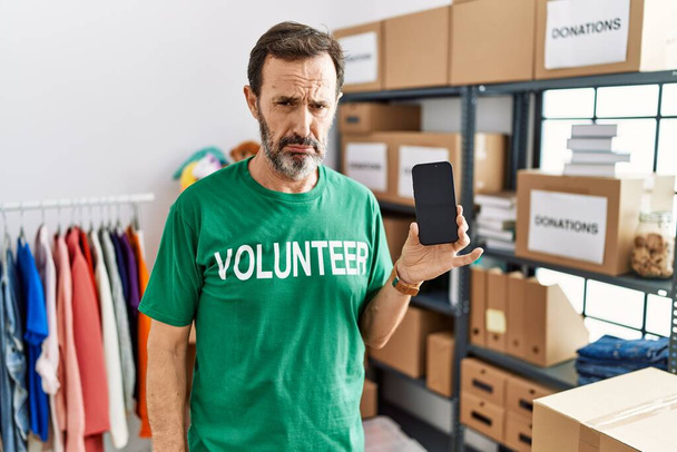 Middle age man with beard wearing volunteer t shirt holding smartphone depressed and worry for distress, crying angry and afraid. sad expression.  - Foto, imagen