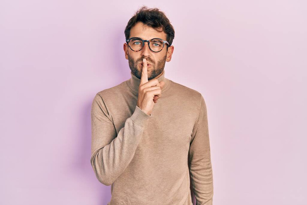Handsome man with beard wearing turtleneck sweater and glasses asking to be quiet with finger on lips. silence and secret concept.  - Photo, Image