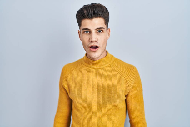 Young hispanic man standing over blue background afraid and shocked with surprise and amazed expression, fear and excited face.  - Foto, afbeelding