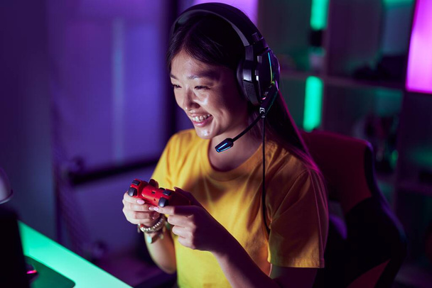 mujer china streamer sonriendo confiado jugando videojuego en la sala de juegos - Foto, imagen