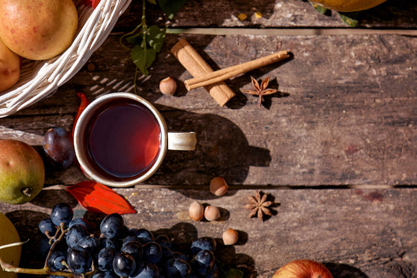Cozy autumn rustic still life: cup of tea, fruits, vegetables, hazelnuts and cinnamon sticks. Autumn aesthetic coziness. Thanksgiving Day concept with place for text - 写真・画像