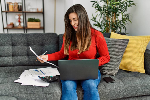 Młoda kobieta korzystająca z laptopa czytającego dokument pracy w domu - Zdjęcie, obraz
