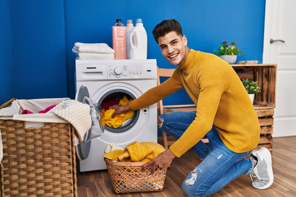 Młody Latynos uśmiecha się pewnie prając ubrania w pralni - Zdjęcie, obraz