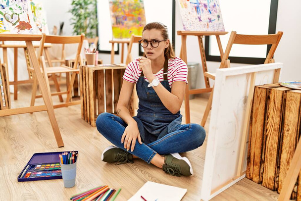 Nuori brunette nainen taide studio istuu lattialla huonovointisuus ja yskä oireena kylmä tai keuhkoputkentulehdus. terveydenhuollon käsite.  - Valokuva, kuva