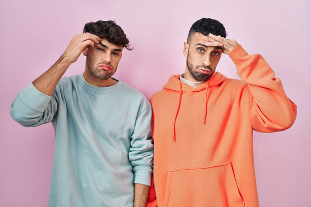 Young hispanic gay couple standing over pink background worried and stressed about a problem with hand on forehead, nervous and anxious for crisis  - Fotografie, Obrázek