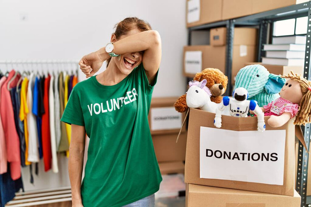 Beautiful caucasian woman wearing volunteer t shirt at donations stand smiling cheerful playing peek a boo with hands showing face. surprised and exited  - Φωτογραφία, εικόνα