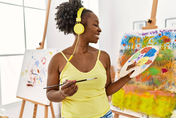 Junge afrikanisch-amerikanische Künstlerin zeichnet mit Kopfhörern im Kunststudio. - Foto, Bild
