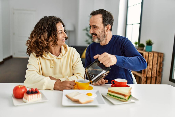 Orta yaşlı İspanyol çift gülümsüyor. Masada oturmuş, evde kahvaltı yapıyorlar.. - Fotoğraf, Görsel