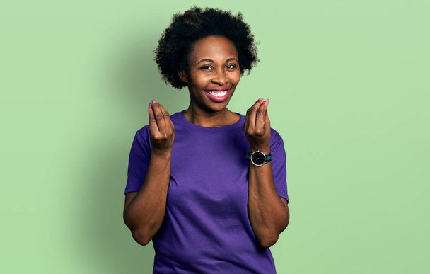 African american woman with afro hair wearing casual purple t shirt doing money gesture with hands, asking for salary payment, millionaire business  - Photo, image