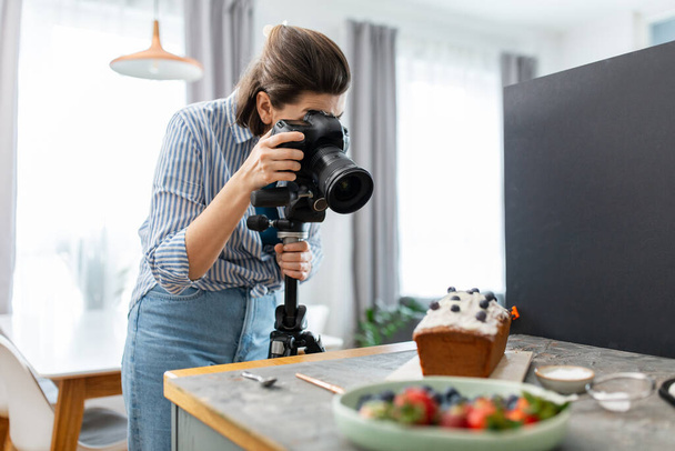 blogging, profession and people concept - happy smiling female food photographer with camera photographing cake in kitchen at home - Fotó, kép