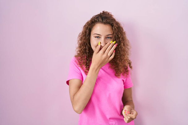 Mujer caucásica joven de pie sobre fondo rosa oliendo algo apestoso y asqueroso, olor intolerable, conteniendo la respiración con los dedos en la nariz. mal olor  - Foto, Imagen