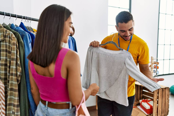 Young latin shopkeeper showing clothes to customer at clothing store. - Foto, Bild