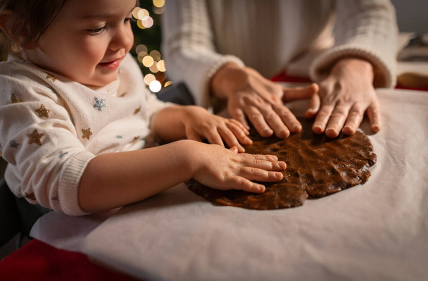 family, cooking and winter holidays concept - happy mother and baby daughter having fun with dough for gingerbread cookies at home on christmas - Foto, Imagen