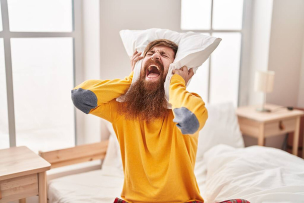 Молодий рудий чоловік прикриває вуха для шуму в спальні
 - Фото, зображення