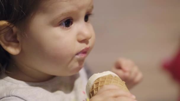 Closeup portrait of cute caucasian baby girl eating licking ice cream in waffle cone. Face and mouth smeared, smeared with cream. - Footage, Video