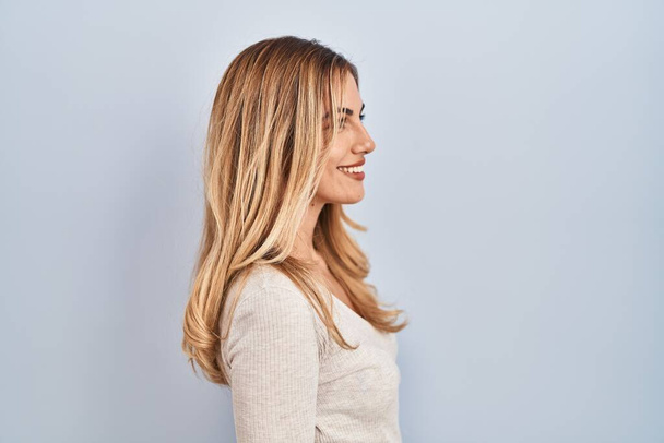 Jeune femme blonde debout sur fond isolé regardant vers le côté, pose de profil relax avec le visage naturel et sourire confiant.  - Photo, image