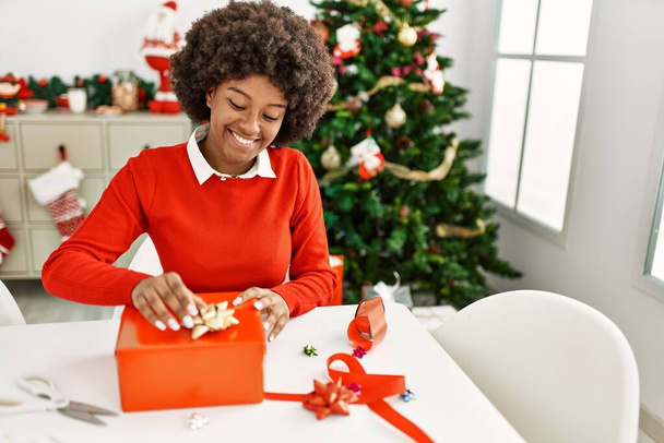 Jeune femme afro-américaine souriante confiante emballage cadeau de Noël à la maison - Photo, image