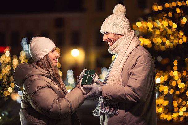 winter holidays and people concept - happy smiling couple with gift over christmas lights in evening - Zdjęcie, obraz