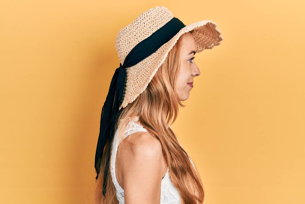 Молода біла жінка в літньому капелюсі дивиться в бік, розслабляє профільну позу з природним обличчям з впевненою посмішкою
.  - Фото, зображення