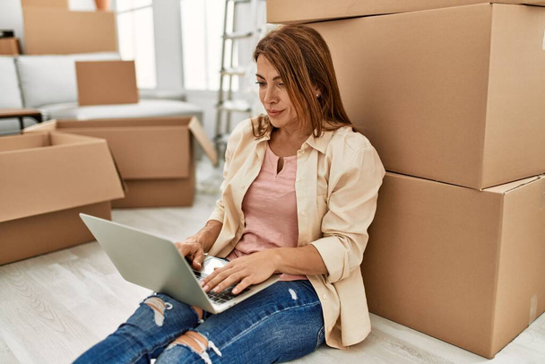 Middle age caucasian woman using laptop sitting on the floor at new home. - Photo, Image