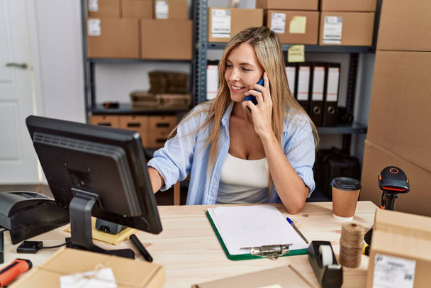 Молодая блондинка электронная торговая бизнес-работница разговаривает по смартфону в офисе - Фото, изображение