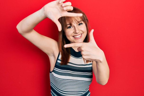 Redhead young woman wearing casual t shirt smiling making frame with hands and fingers with happy face. creativity and photography concept.  - Fotó, kép