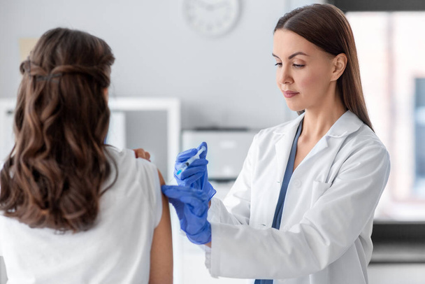 здоровье, медицина и пандемическая концепция - женщина-врач или медсестра в защитных медицинских перчатках со шприцем, вакцинирующим пациента в больнице - Фото, изображение
