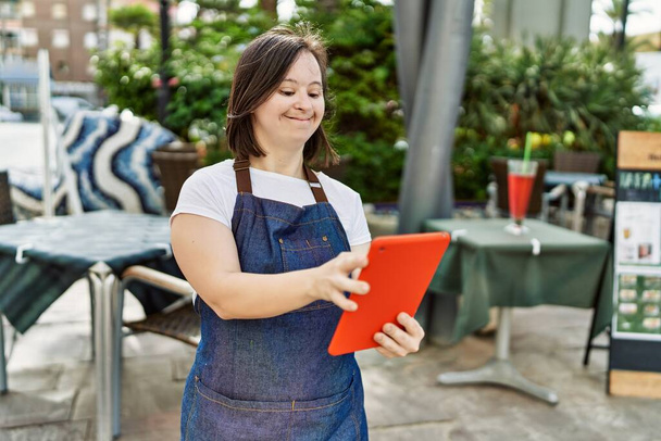 Young down syndrome woman wearing apron using touchpad at coffee shop terrace - Photo, Image