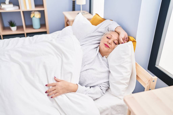 Middle age blonde woman sleeping lying on bed at bedroom - Photo, Image