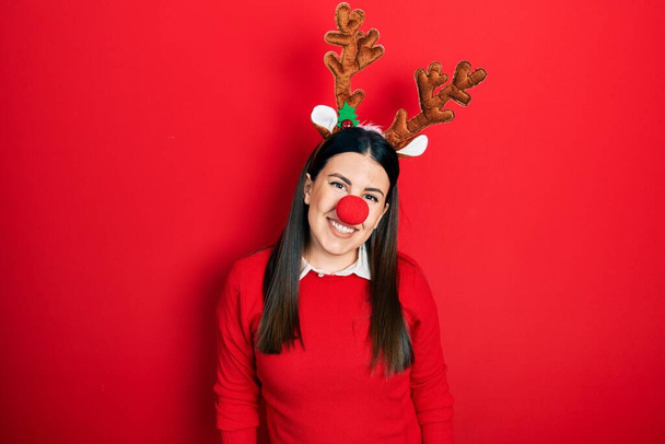 Young hispanic woman wearing deer christmas hat and red nose with a happy and cool smile on face. lucky person.  - Photo, Image