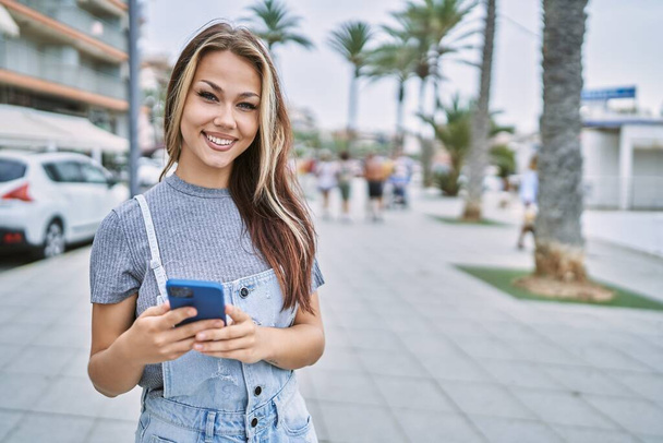 Genç beyaz kız şehirde akıllı telefon kullanarak mutlu bir şekilde gülümsüyor.. - Fotoğraf, Görsel